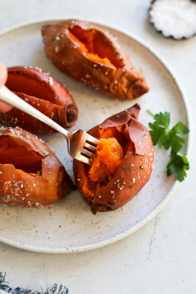 Baked sweet potatoes on a stone plate, a gold fork lifting up forkful of fluffy sweet potato