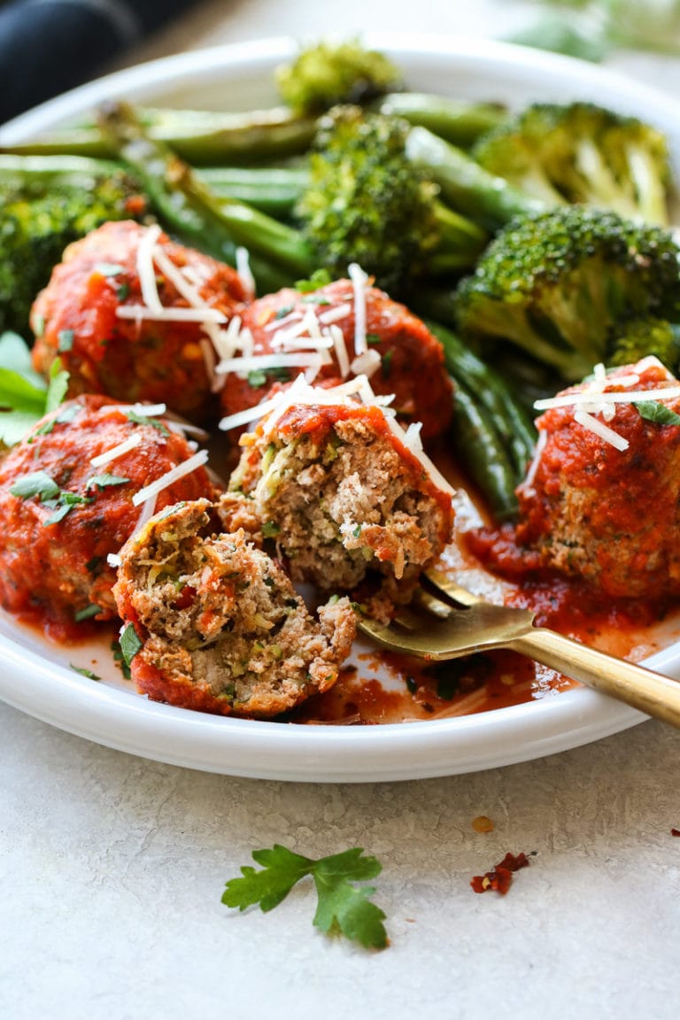 Side view turkey meatballs in red sauce on plate with roasted broccoli