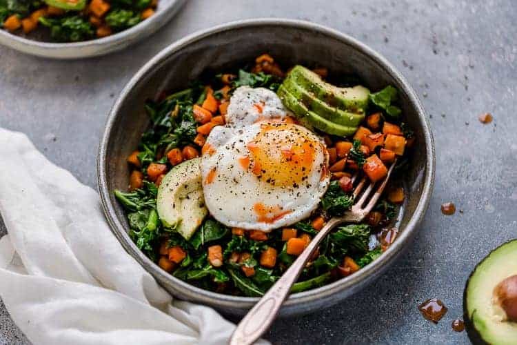 Kale and sweet potato sauté in a stone bowl topped with fried egg and hot sauce.