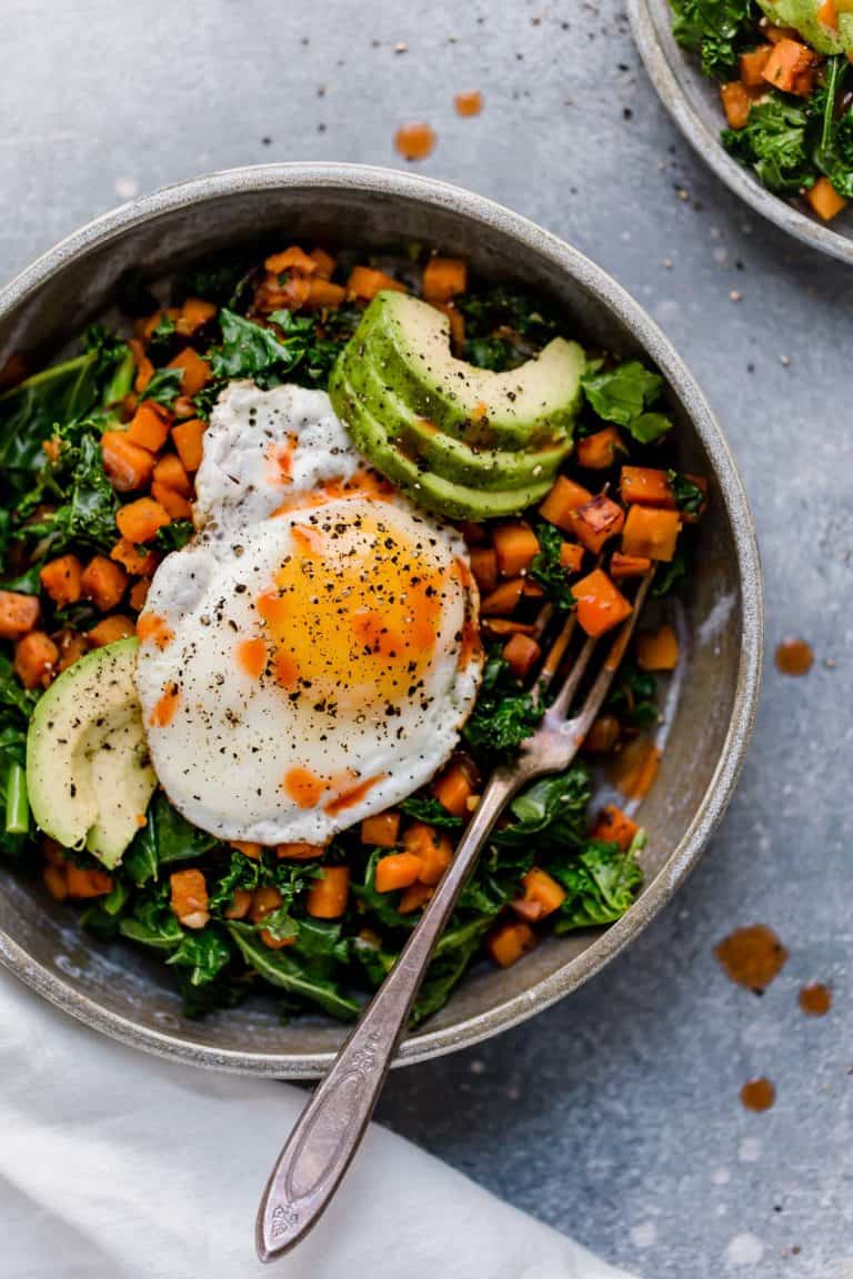 Overhead view of a plate of kale and sweet potato sauté topped with a fried egg. 