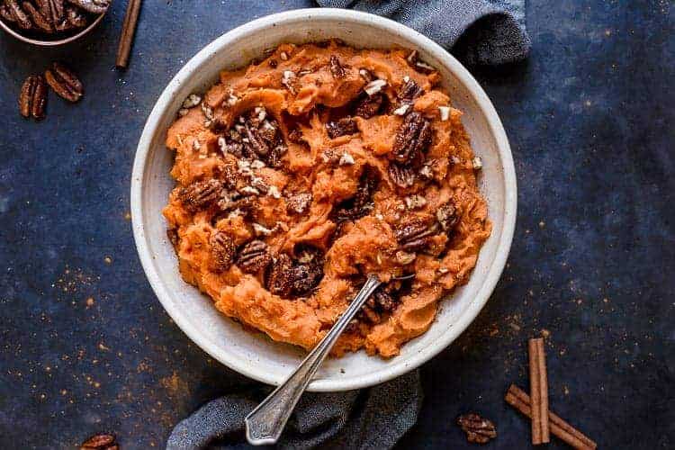 Creamy maple mashed sweet potatoes in a white serving bowl topped with pecans.