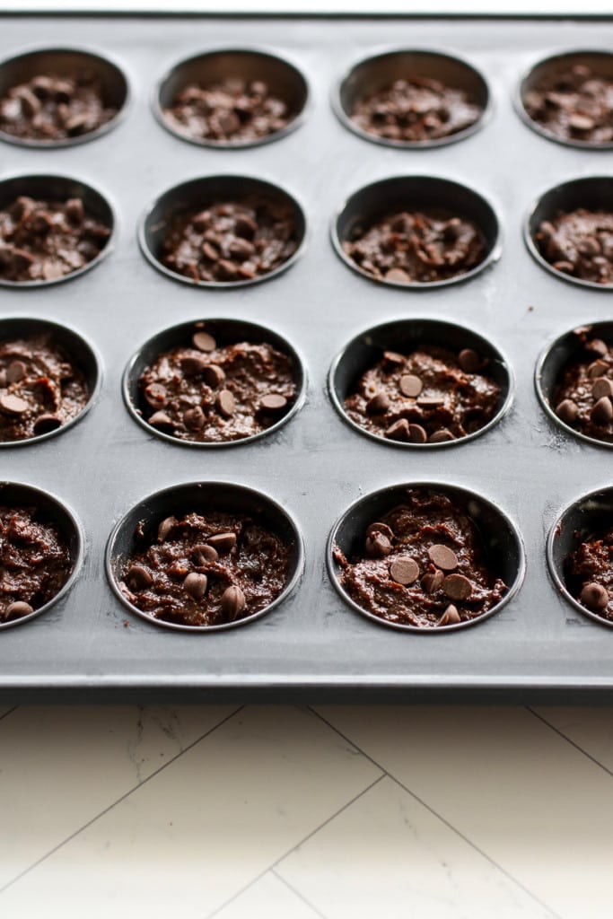 A mini muffin tin filled with brownie bite batter, a few mini chocolate chips sprinkled on top of each.