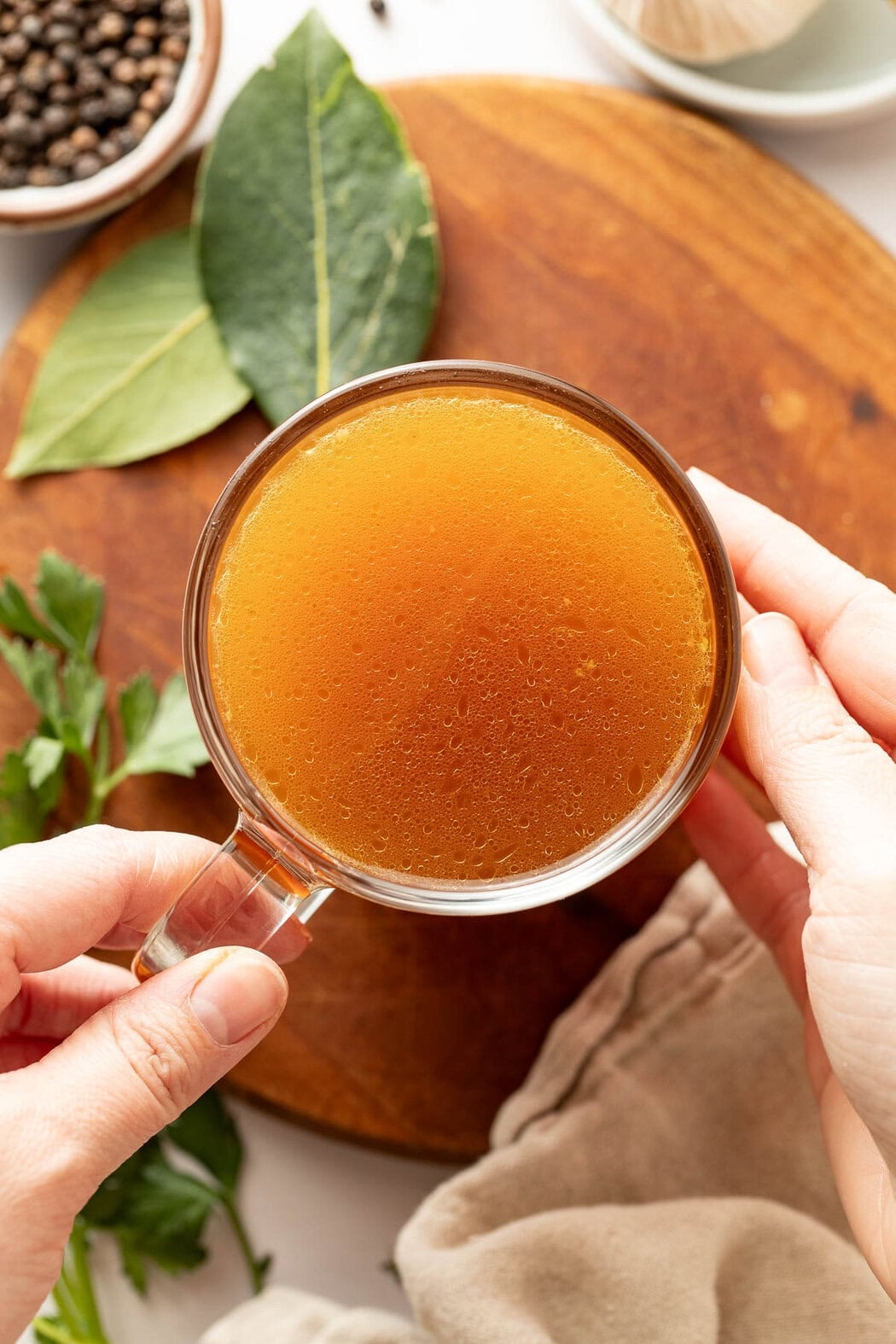 Overhead view of hands holding a glass mug of bone broth.