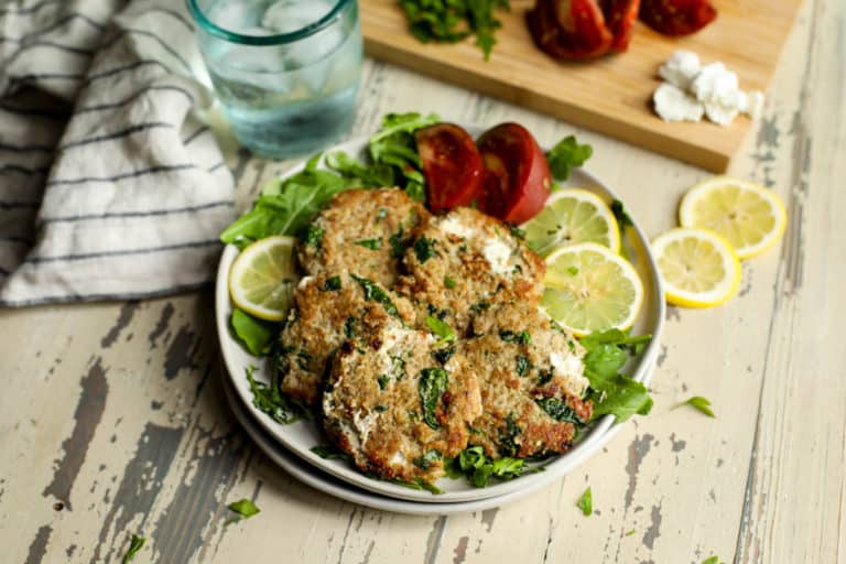 Quinoa spinach turkey burgers with goat cheese on serving plate over lettuce leaves with lemon slices and tomato wedges. 