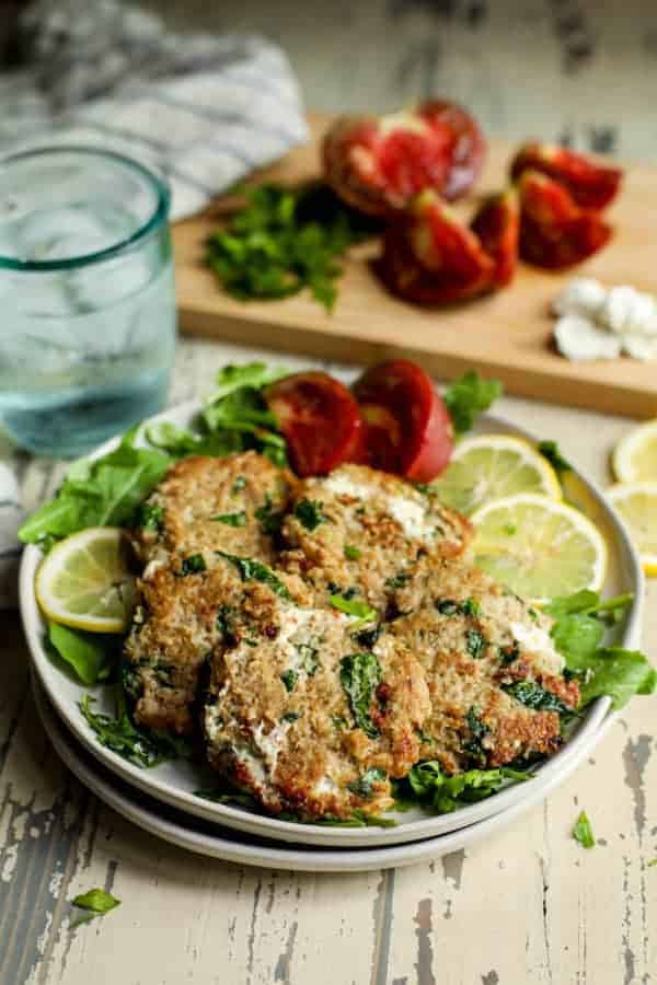 Quinoa Spinach Turkey Burgers with Goat Cheese on a plate with greens and tomato wedges and lemon slices