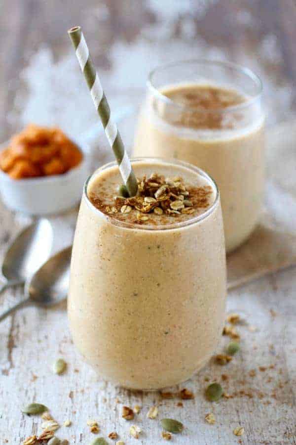 Pumpkin Pie Protein Smoothie in a glass topped with granola and a gray and white straw