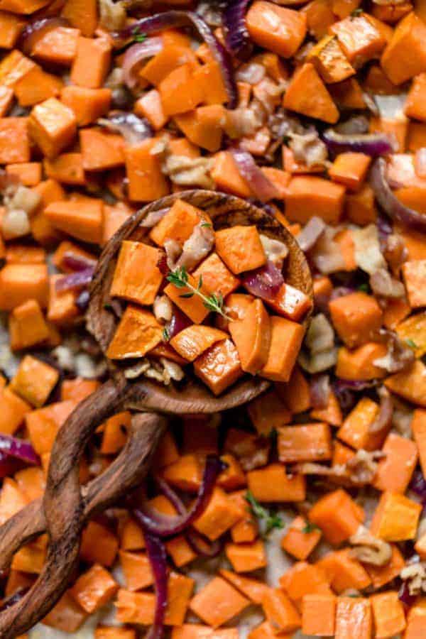 A spoonful of Roasted Sweet Potatoes with Maple and Bacon resting on a sheet pan full