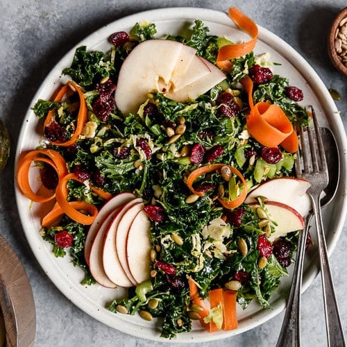 Massaged Kale Salad topped with sliced apples and carrots.