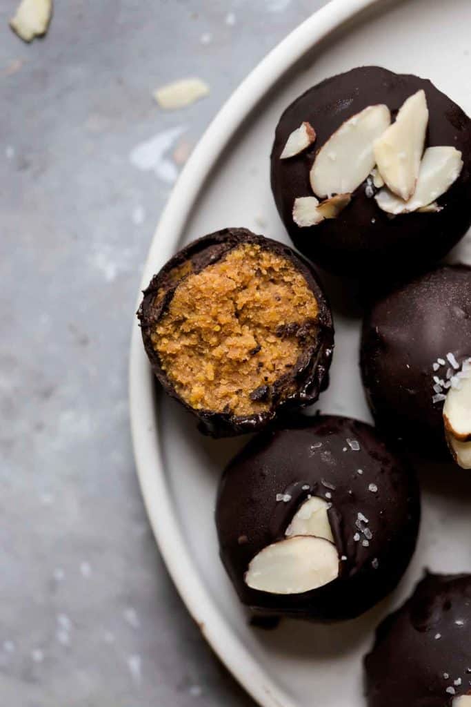Several pumpkin pie truffles coated in dark chocolate topped with slivered almonds on white plate. 