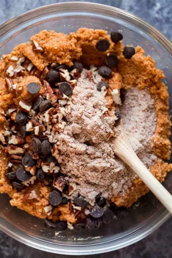 Paleo pumpkin bread batter in a glass bowl being stirred with a wooden spoon.