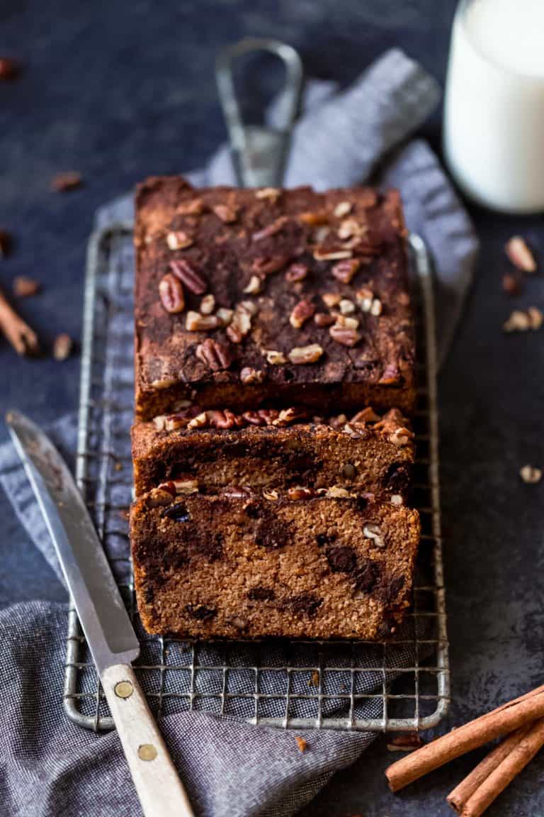 A cooling rack with a freshly baked Pumpkin Chocolate Chip Bread loaf on it topped with chocolate pieces and chopped nuts. 