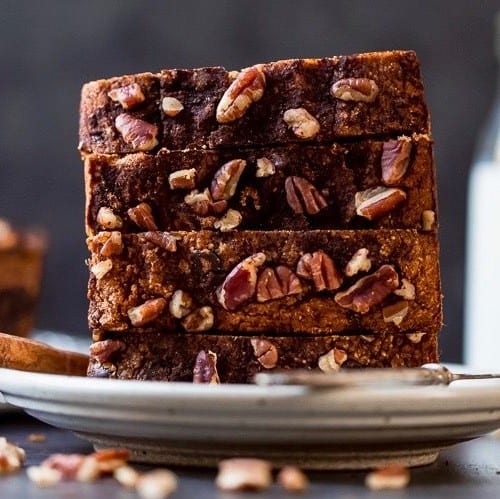 Slices of Healthy Paleo Pumpkin Bread with chocolate chips and pecans stacked up on a cream plate with a pitcher of milk in the background.