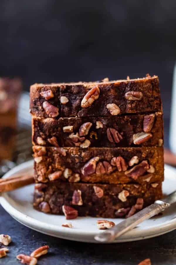 Four thick slices of healthy pumpkin bread stacked on top of each other on a cream plate.