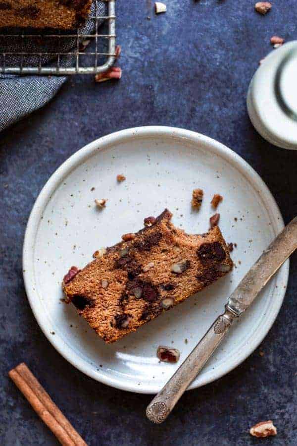 Overhead view of a Pumpkin Chocolate Chip Bread slice missing a bite on a white plate with a knife laying next to it 