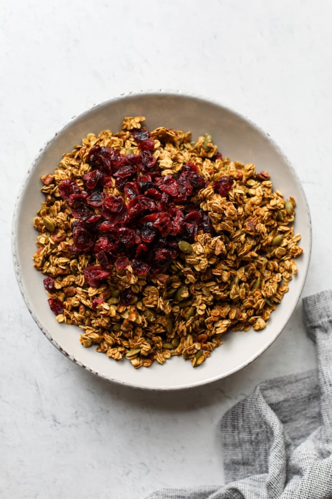 Pumpkin granola freshly baked in a white serving bowl with dried cranberries poured on top
