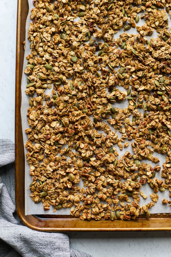 Pumpkin spice granola with chopped pecans and pumpkin seeds on a parchment-lined baking sheet.