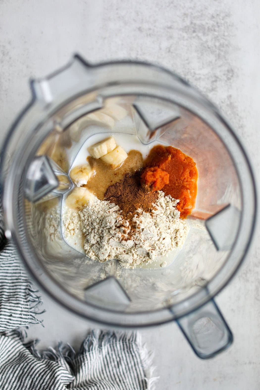 Overhead view into a blender of all the ingredients for a Delicious Protein Pumpkin Spice Smoothie ready for blending. 