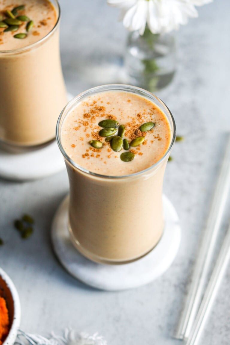 two glasses filled with protein pumpkin smoothies topped with cinnamon and pepitas.