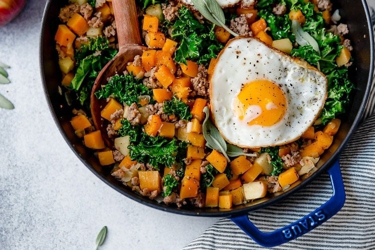 Butternut squash and apple hash with sausage in skillet with fried egg on top