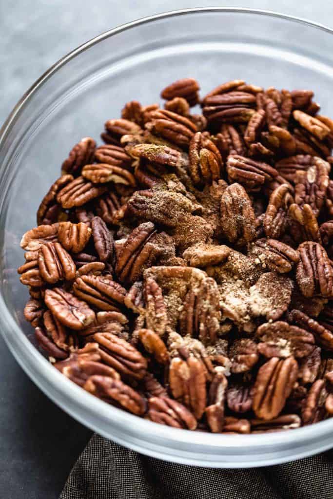 Pecans in a clear glass bowl with maple syrup and cinnamon on top