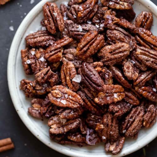 Overhead view spiced pecans sprinkled with flaky sea salt on white plate