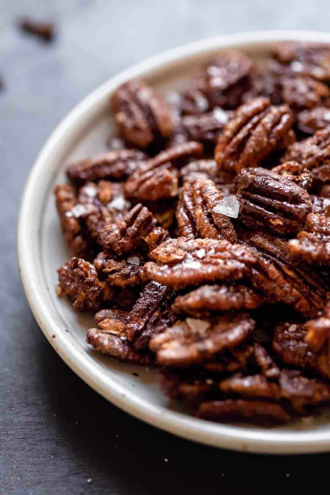 Close up view Spiced Pecans on a white plate sprinkled with flaky sea salt