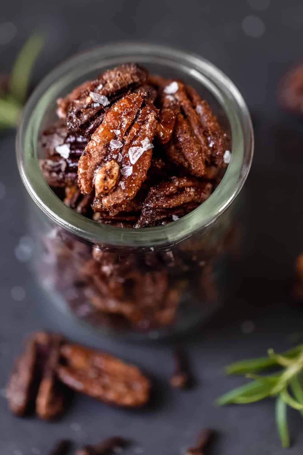 Close up view spiced pecans coated in sugar maple syrup and sprinkled with flaky sea salt in small glass jar