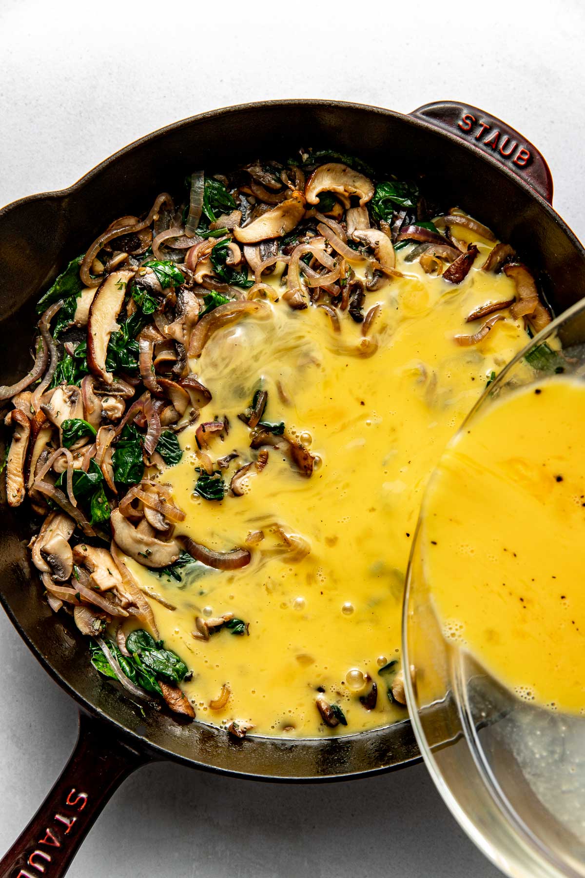 Overhead view of a pan filled with Mushroom Frittata ingredients with eggs being poured on top. 