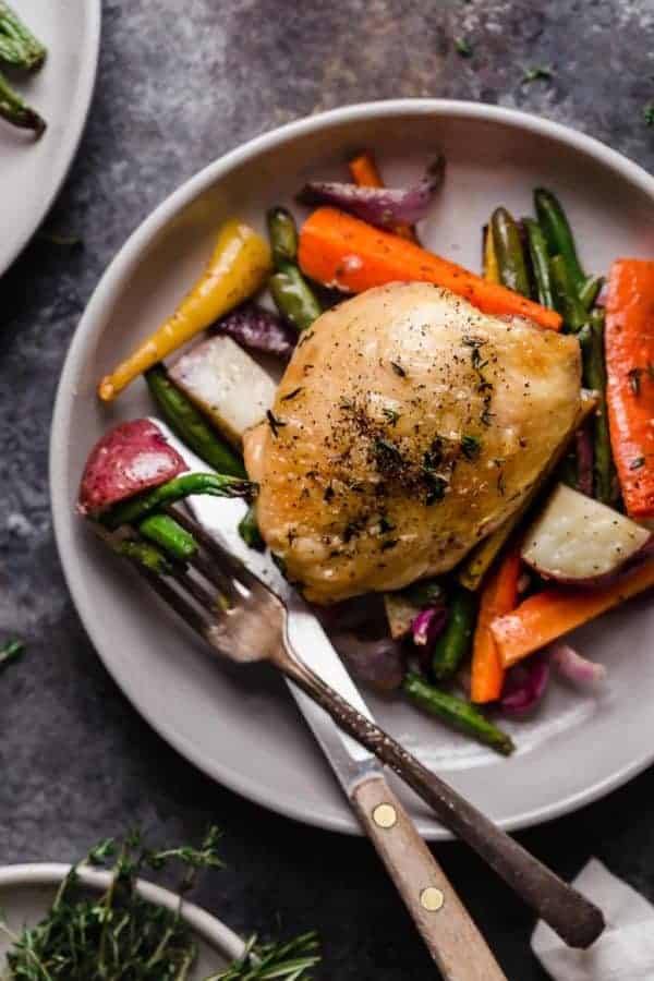 Overhead view sheet pan chicken and veggies served on plate with silver cutlery.