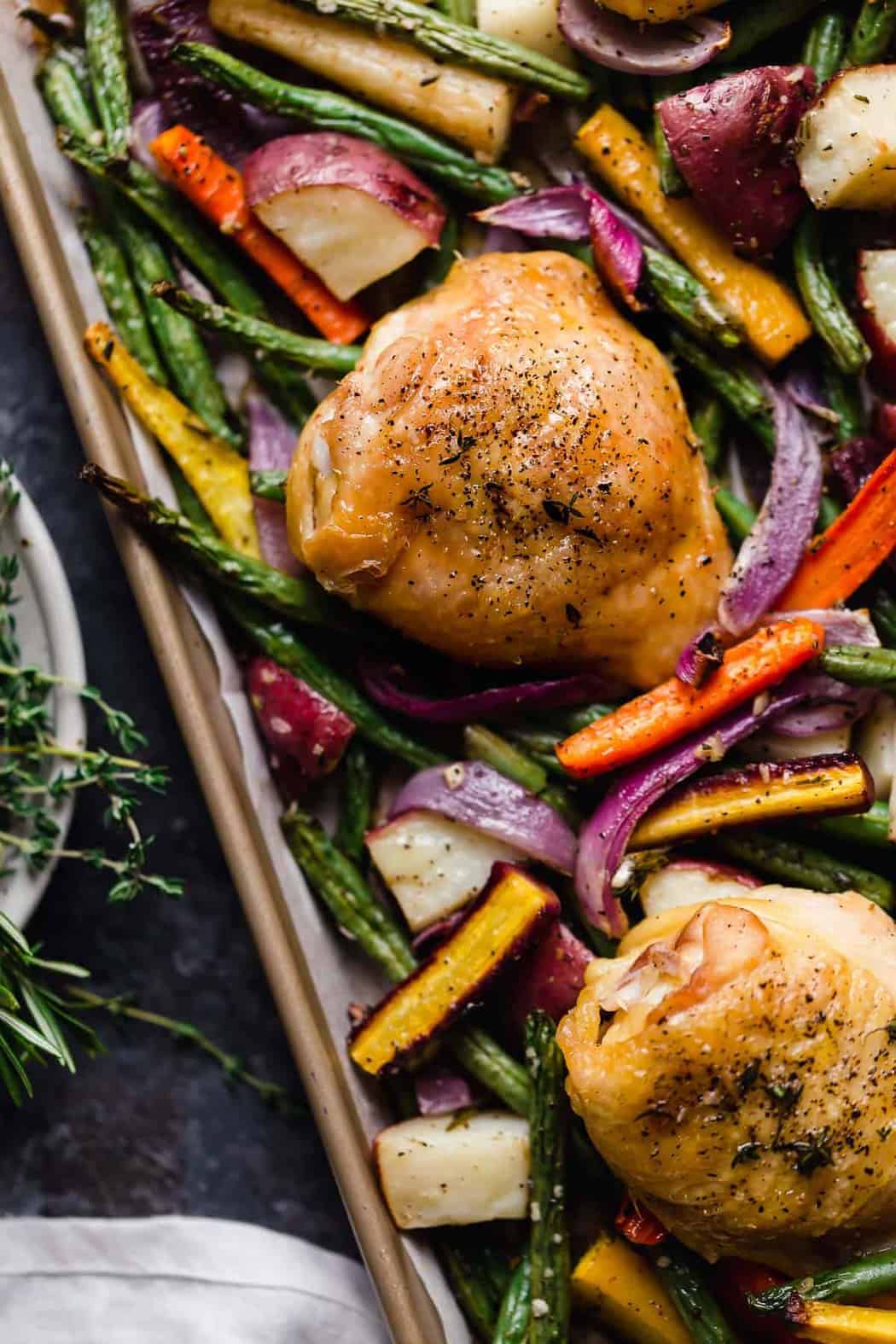 Sheet pan filled with baked chicken thighs and a rainbow of vegetables