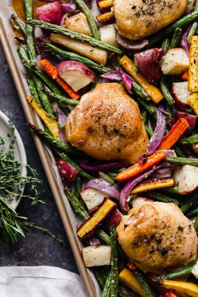 Close up overhead view chicken thighs and vegetables on sheet pan.