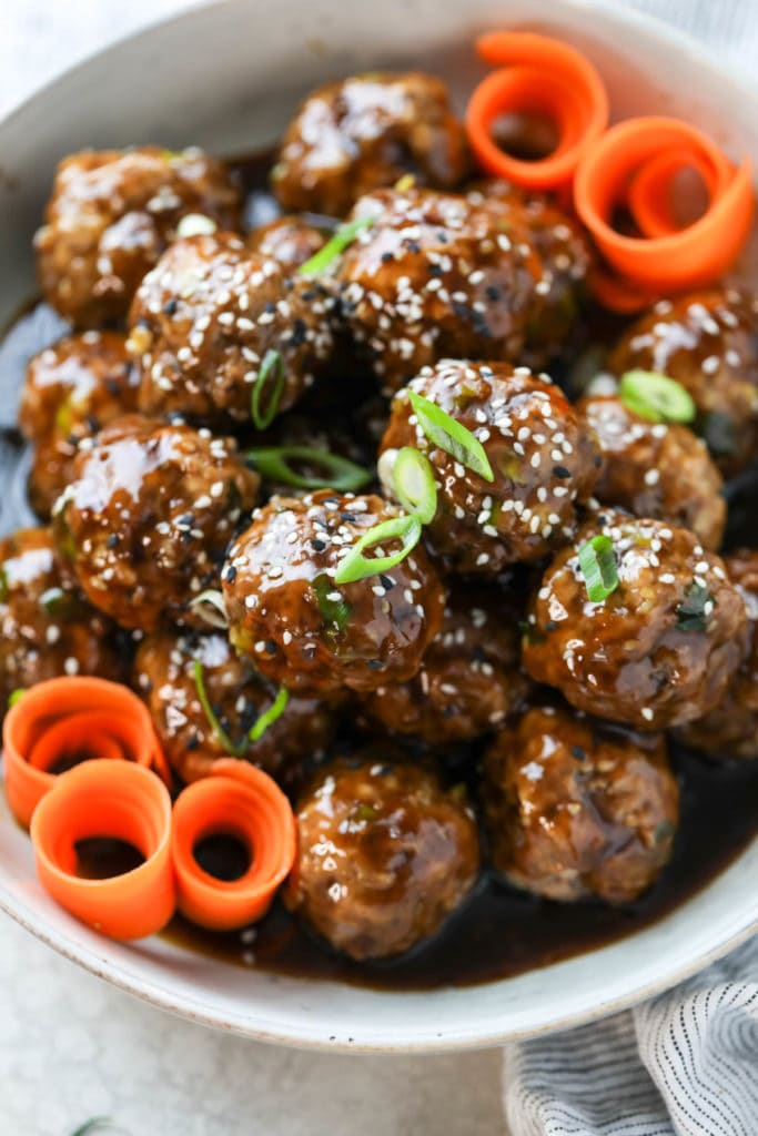 Teriyaki Meatballs in a serving bowl sprinkled with sesame seeds and carrots swirls. 