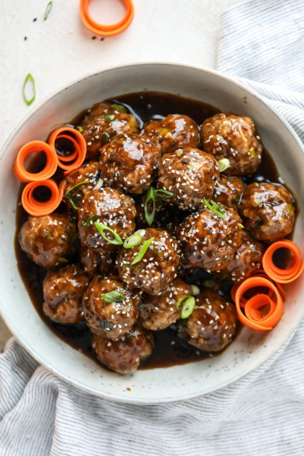 A bowl full of teriyaki meatballs topped with sesame seeds and scallions