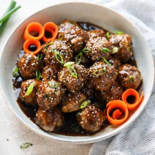 Teriyaki meatballs coated in homemade teriyaki sauce served in a white bowl topped with sesame seeds