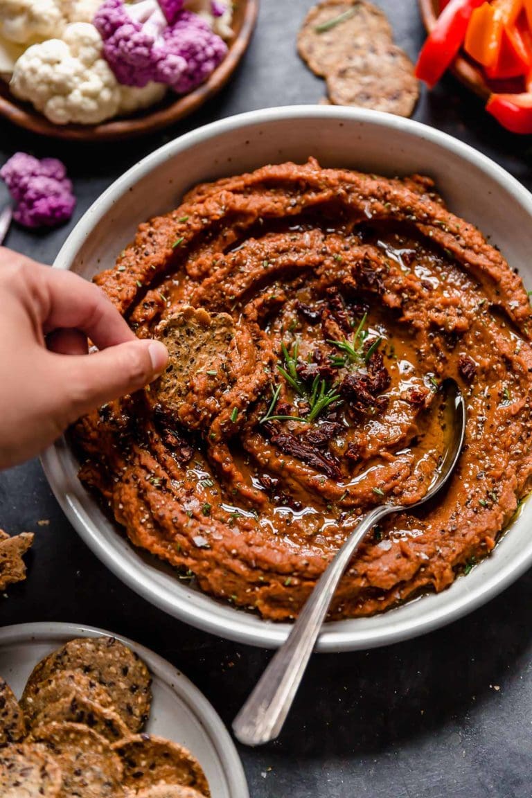 A cracker being dipped into Tuscan white bean dip served in shallow bowl