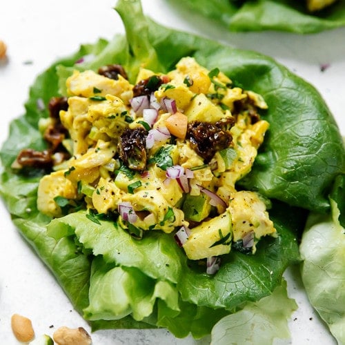 Curry chicken salad in lettuce leaves topped with raisins and cashews.