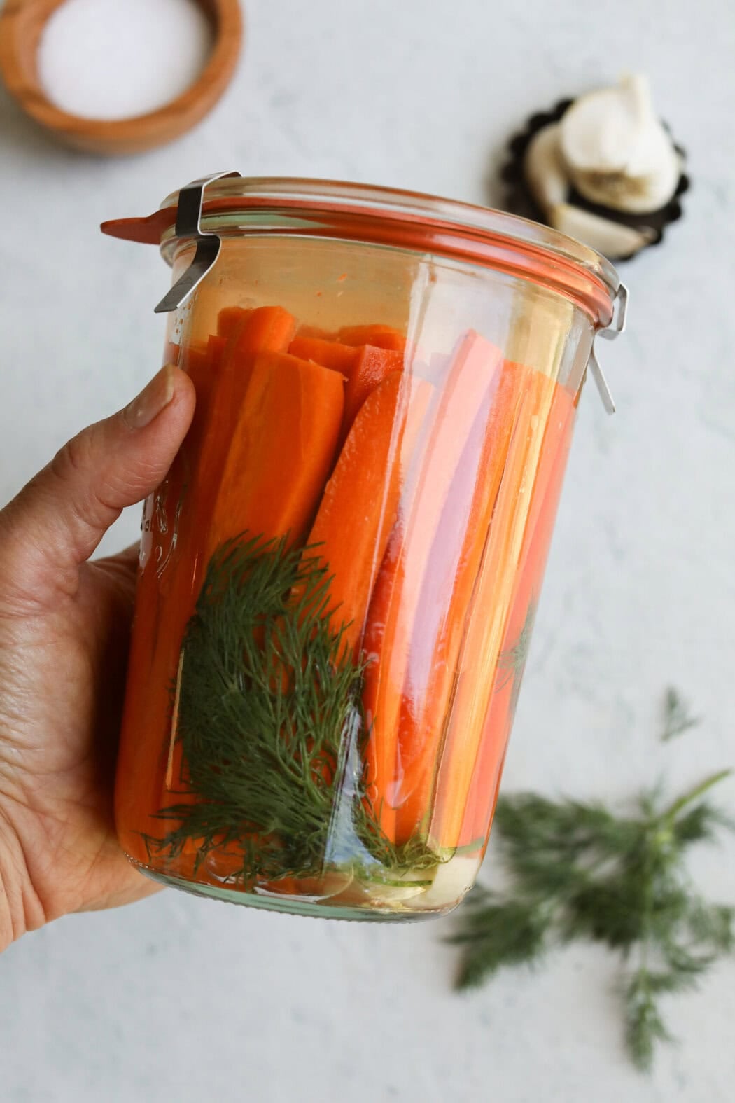 A hand holding a jar of pickled carrots submerged in liquid. 