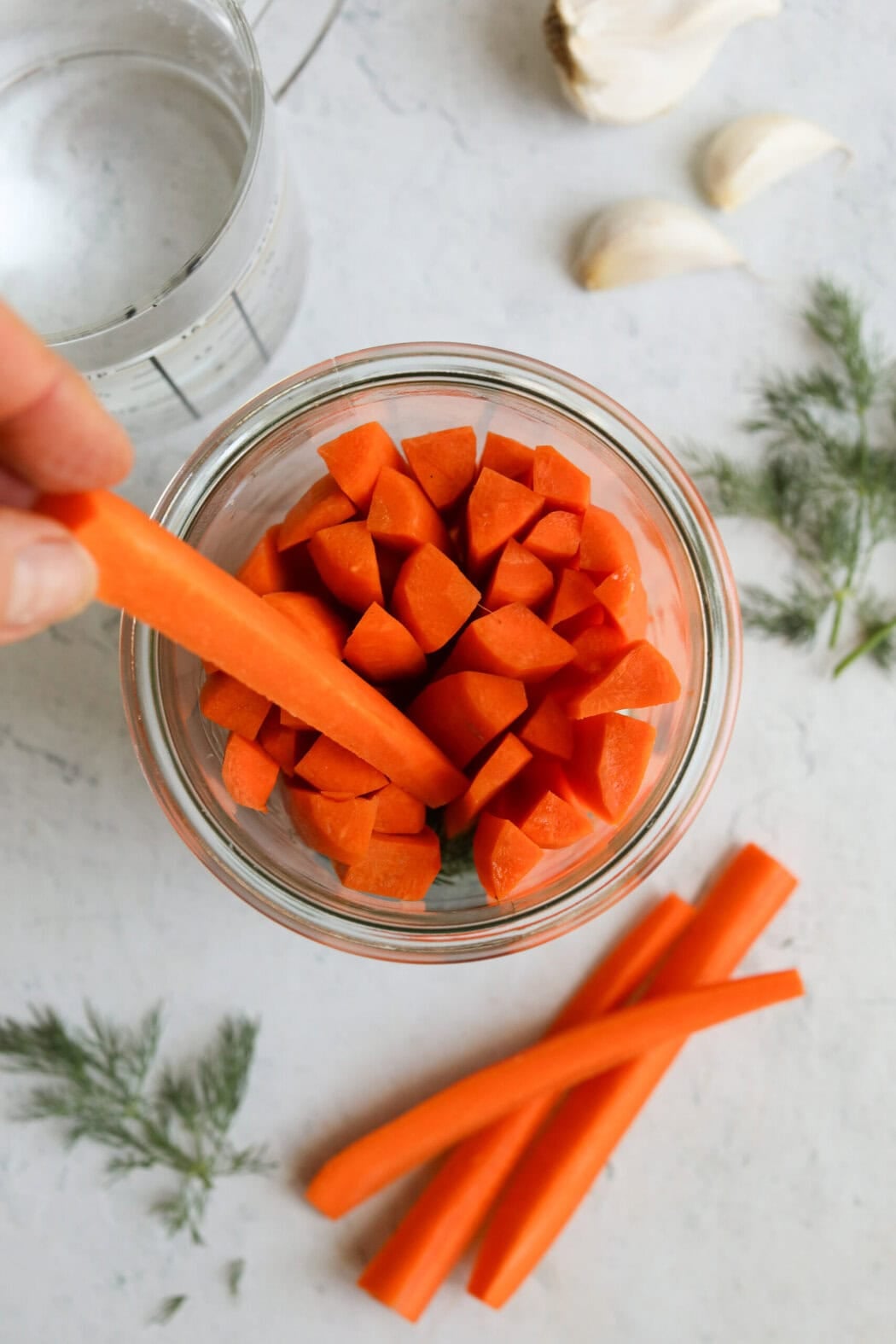 A hand putting carrot sticks in a Weck jar. 