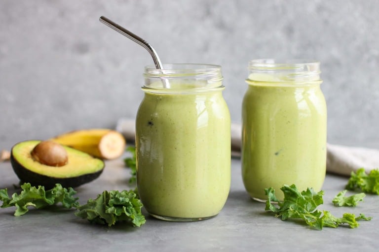 Close up view of a mason jar filled with a green smoothie and a straw stuck in the jar.