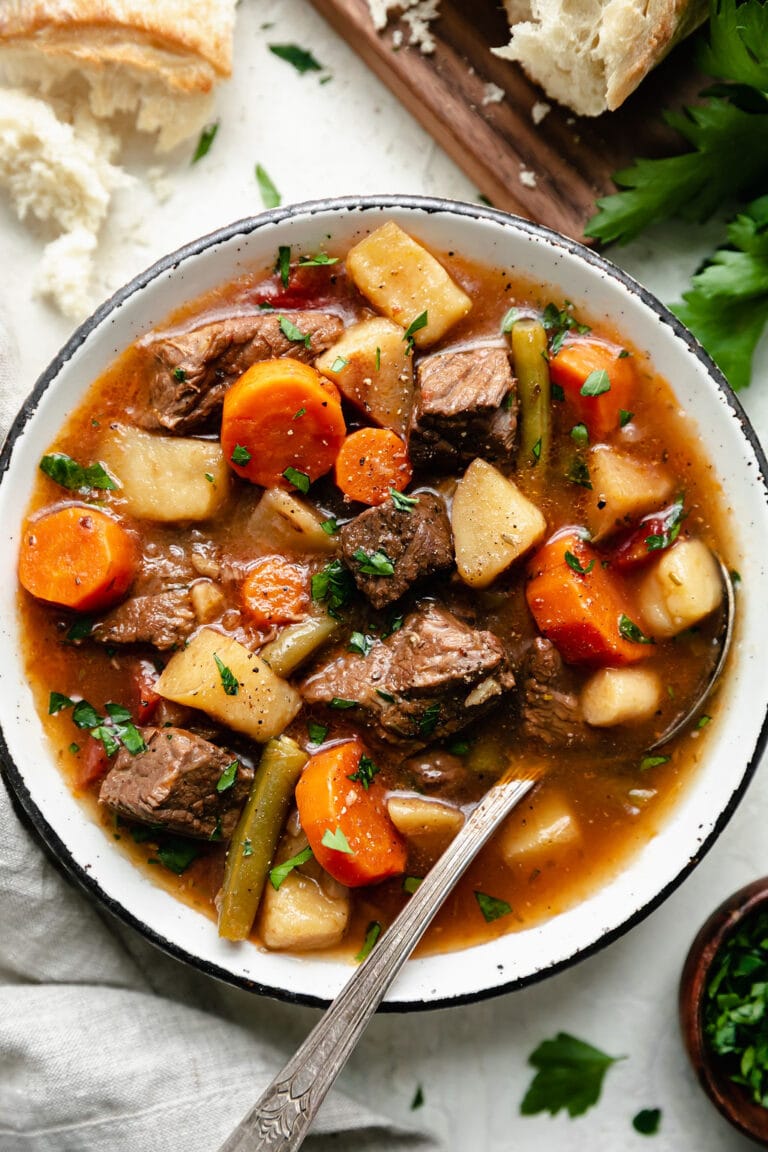 Overhead view rustic white bowl filled with slow cooker beef stew with root vegetables