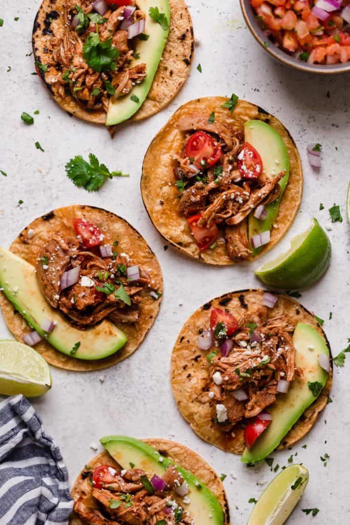 Shredded chicken taco meat on corn tortillas with avocado sliced and taco fixings