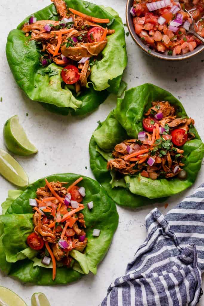 Three butter lettuce leaves filled with shredded chicken taco meat and taco toppings.