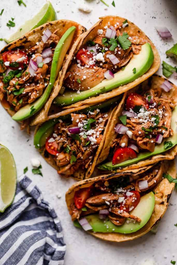 Five chicken tacos in corn shells with avocado slices and white cheese.