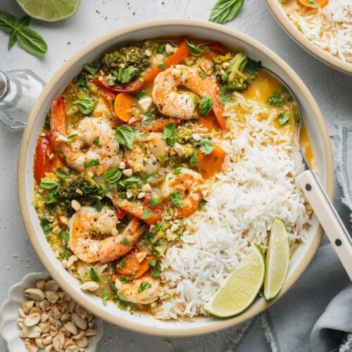 A bowl of coconut curry shrimp soup and rice, a spoon sticking out.