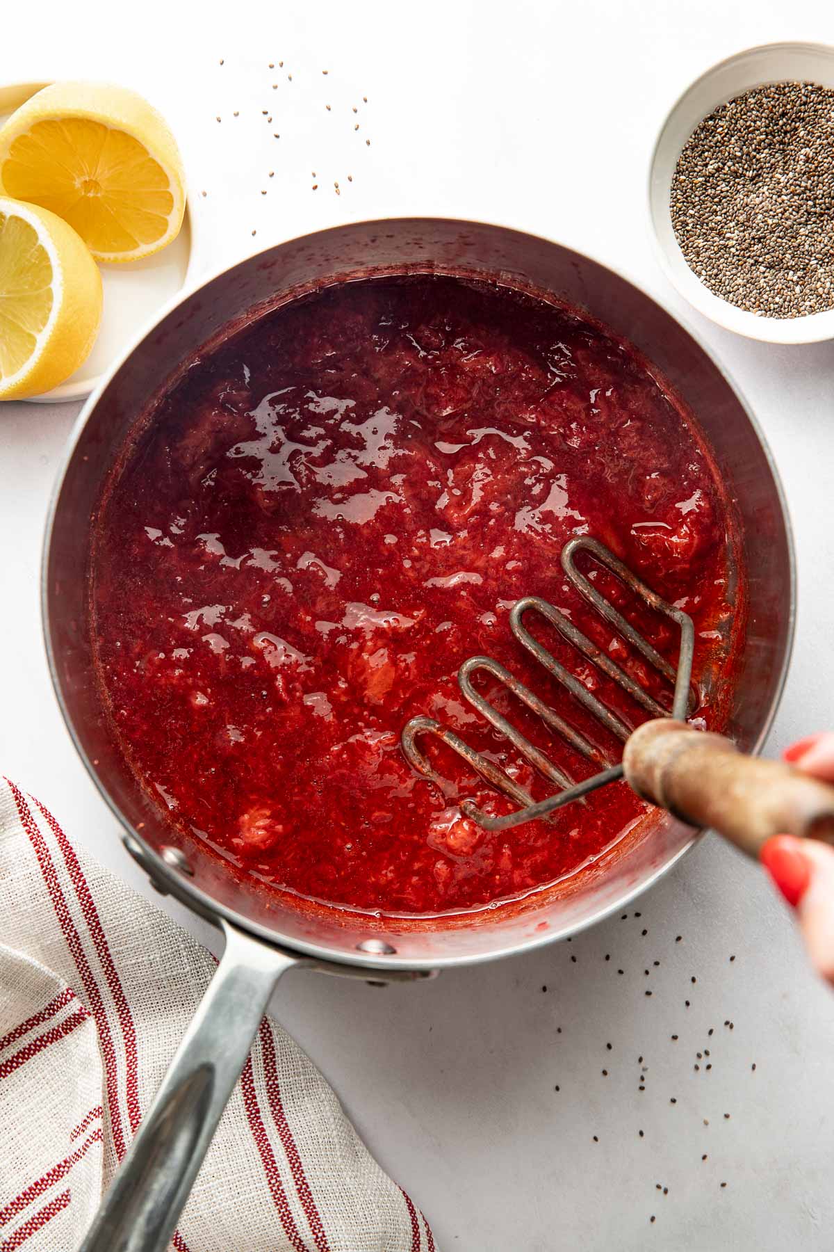 Overhead view of a small pot filled with Chia Seed Jam Strawberry mixture with a masher in the pan.