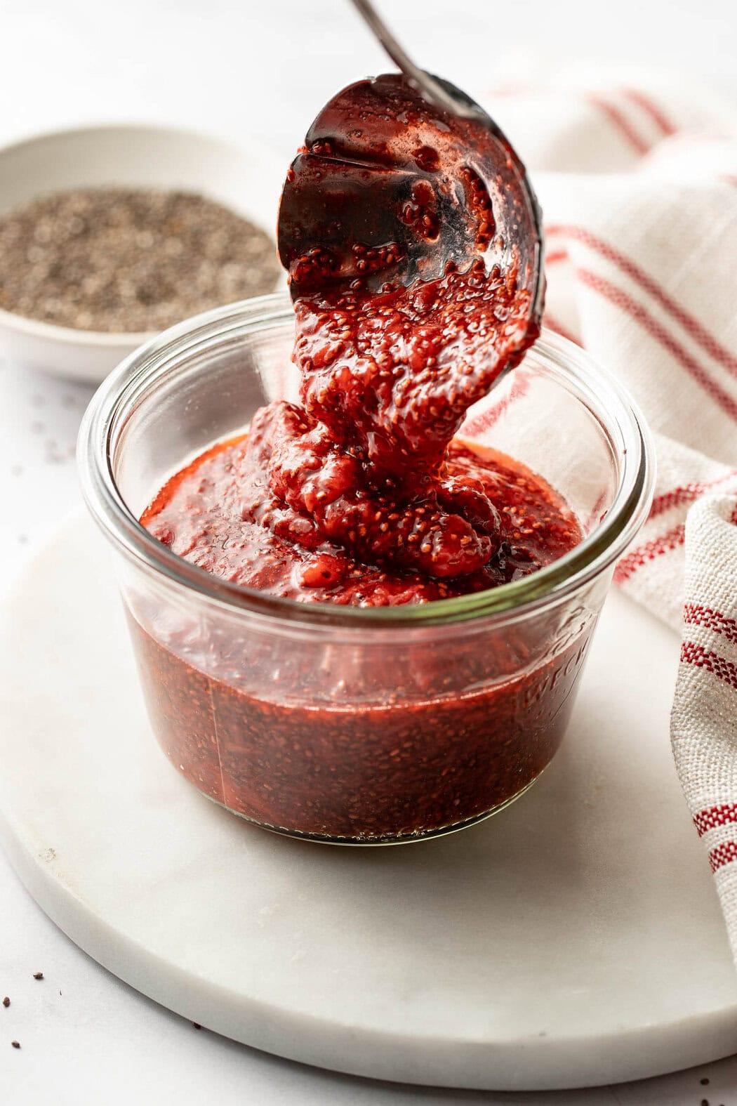 Close up view of a small ladle spooning fresh Chia Seed Jam into a small glass jar.