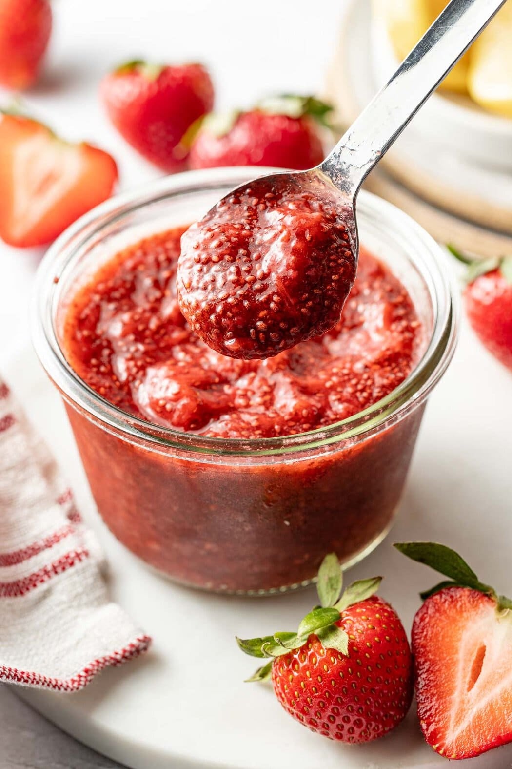 Close up view of a small glass jar of red Chia Seed Jam with a spoon bringing up a scoop.