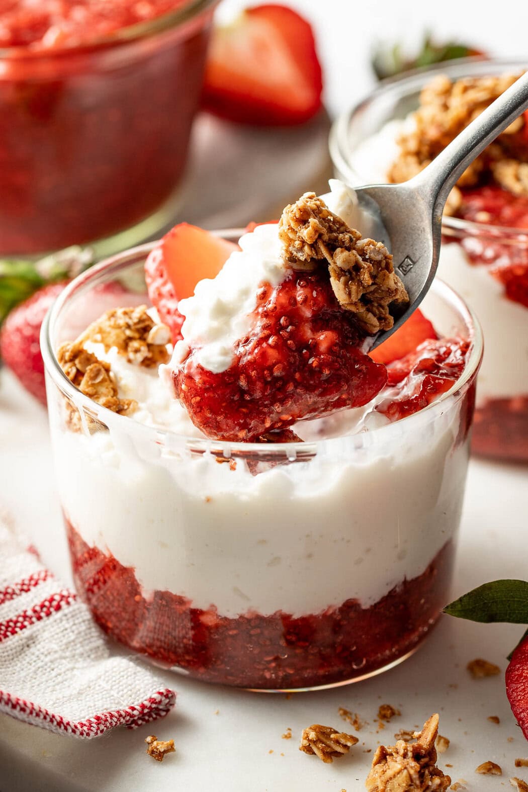 Side view of a small glass jar showing layers of Chia Seed Jam and yogurt with granola sprinkled on top.