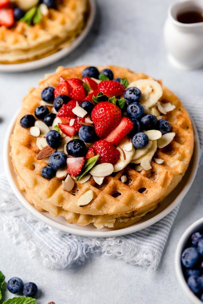 A stack of Crispy Grain-Free Waffles topped with fresh berries, bananas, and almond slices. 