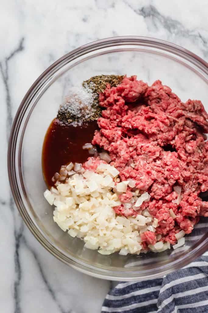 Overhead view ground beef in a mixing bowl with chopped onions, bbq sauce, and seasoning. 